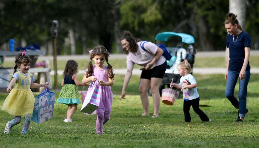 Young children running across a park lawn with baskets